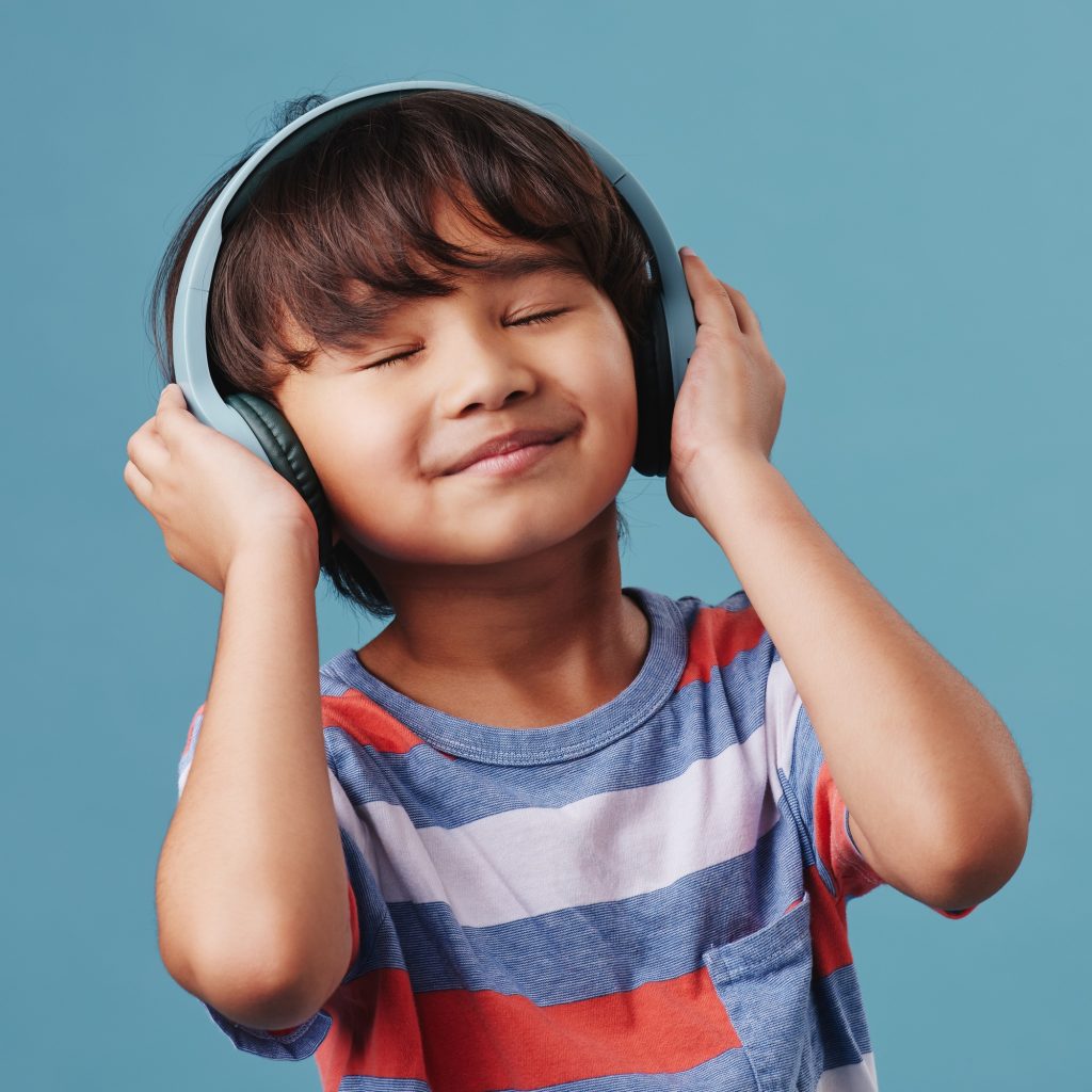 A cute young asian boy enjoying listening to music from his wireless headphones. Adorable Chinese k