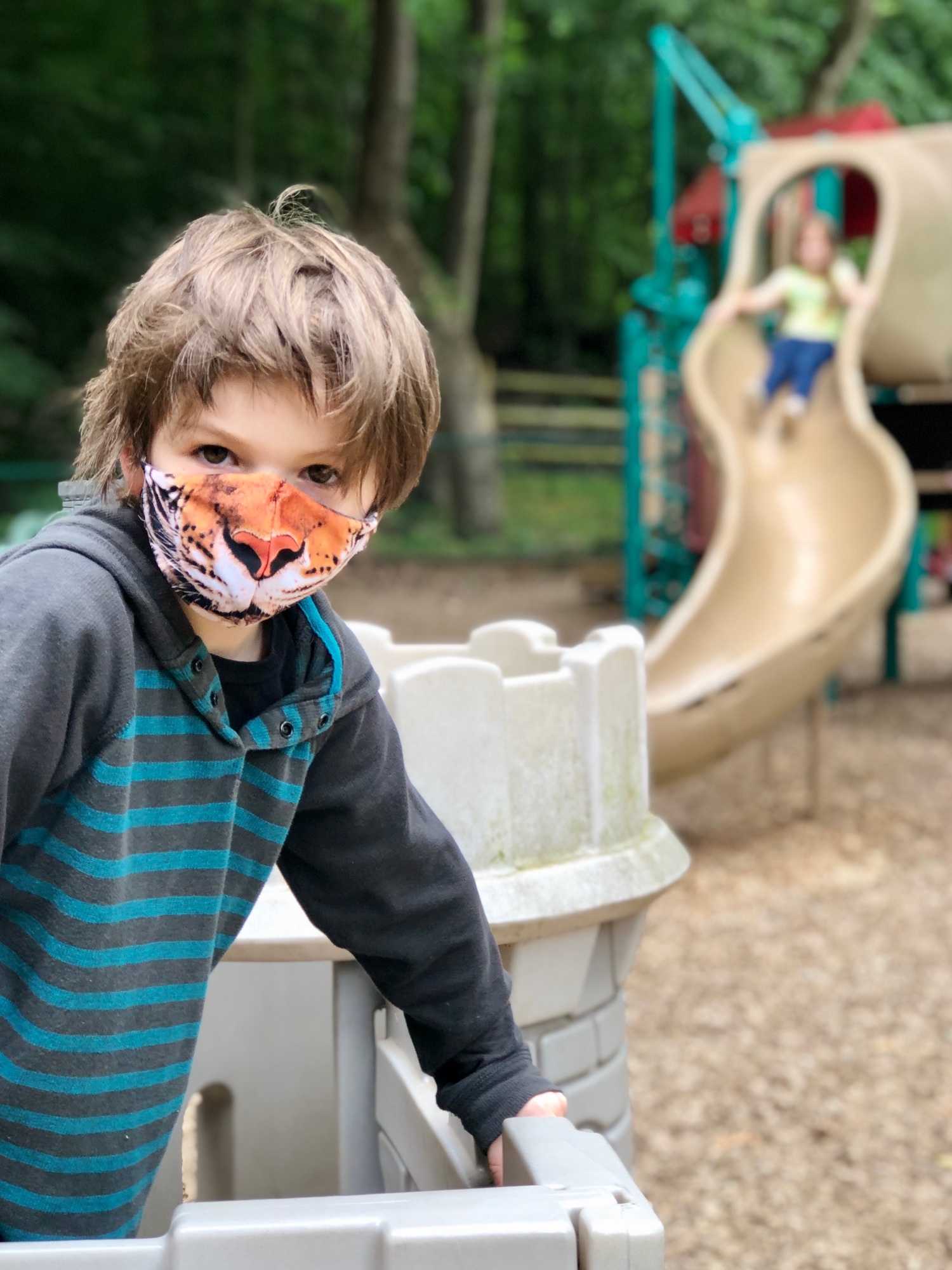 Boy on playground with face mask looking at camera on socially distanced from other kids