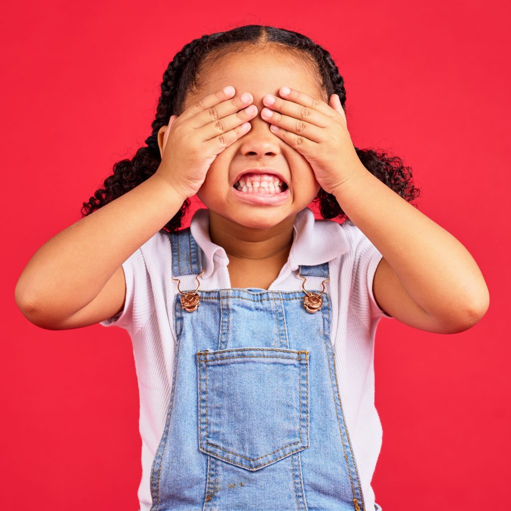 Child, hands and eyes cover on isolated red background with angry, mad or stubborn facial expressio