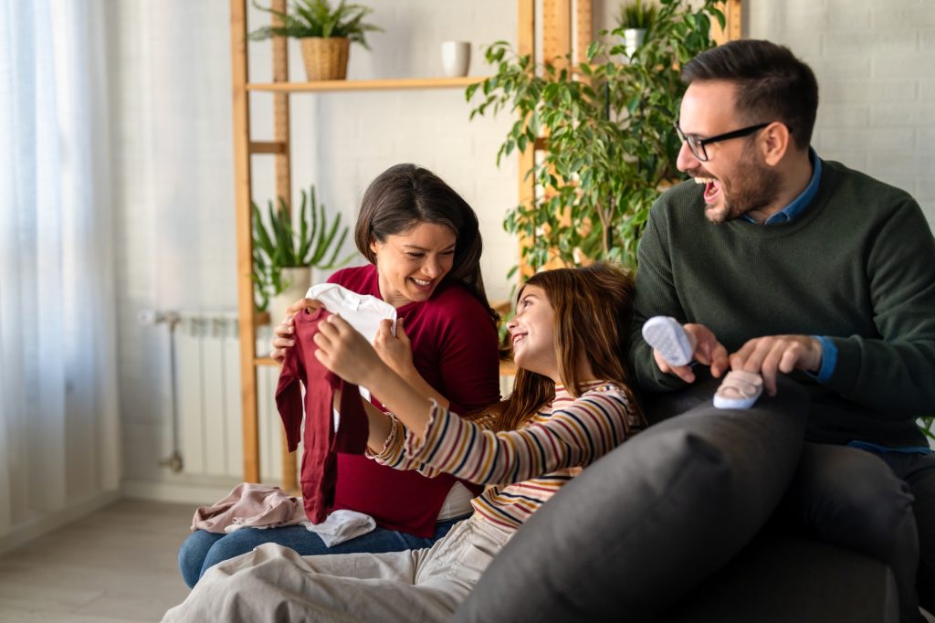 Happy parents with kid preparing baby clothes while looking at the ultrasound scan photo of baby