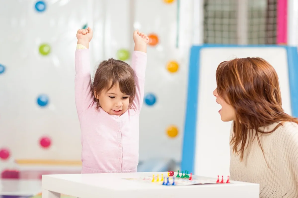 Girl raising her arms with excitement next to her therapist during an activity